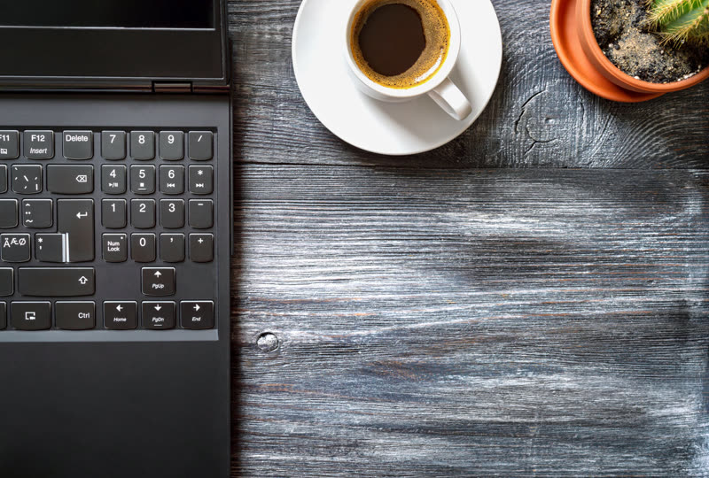 A laptop, an espresso cup and a cactus on a weathered wooden table