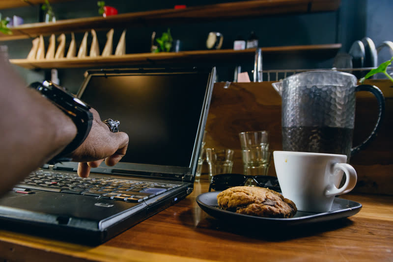 Someone typing on a laptop beside a cookie and a cup of coffee