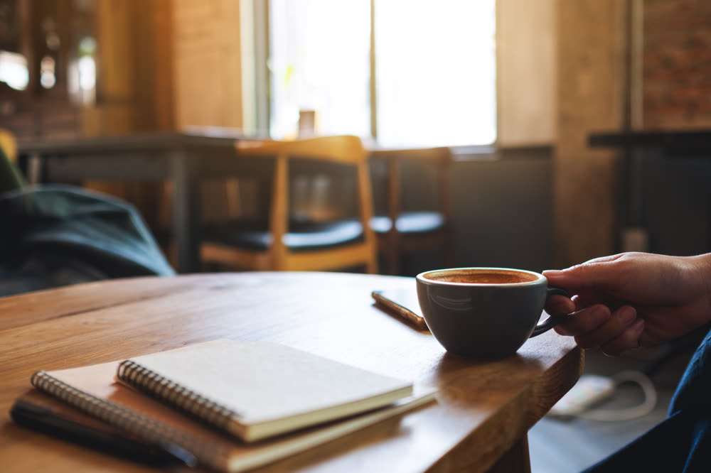 A cup of coffee beside a spiral notebook on a cafe table