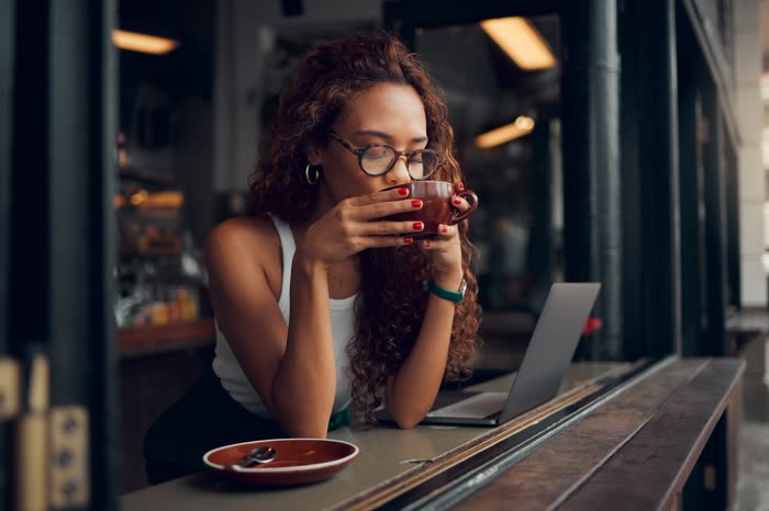 A woman sipping coffee at a cafe window with her laptop