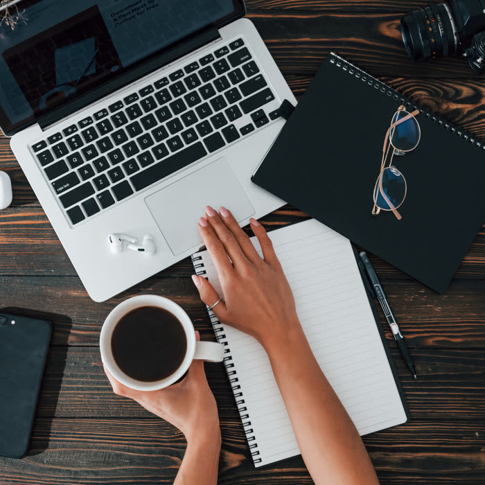 Hands on a laptop and notebook beside a cup of coffee, seen from above