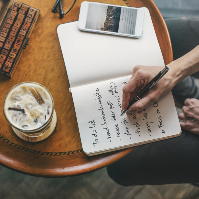 Writing a to-do list beside an iced coffee and a phone