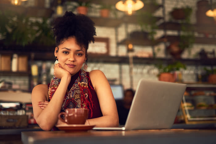 A woman with her chin on her hand at a cafe counter beside her laptop